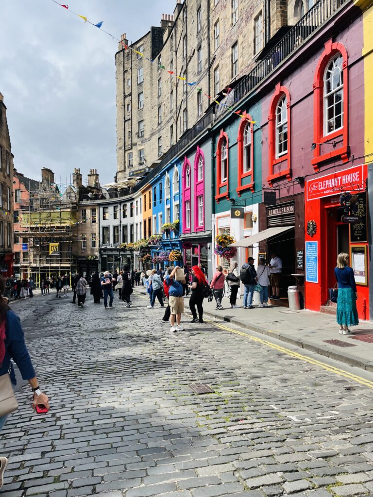 This image pictures Victoria Street, one of the most iconic streets in Edinburgh. There are beautiful colored shops along the street. 